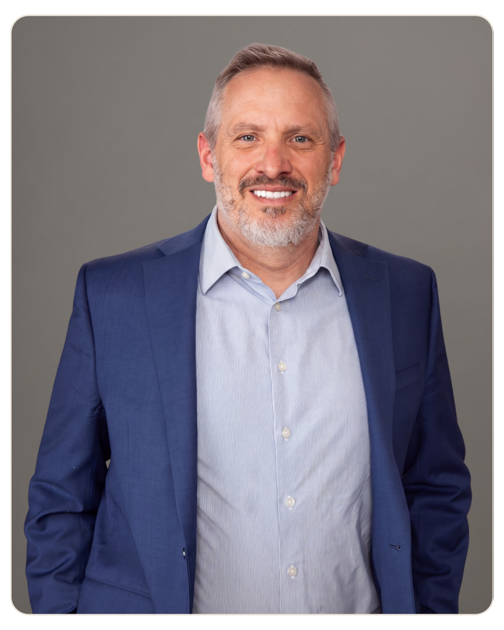 Andrew Ozmun Smiling middle-aged man in a blue blazer and light blue shirt, posed for a professional headshot against a gray background.