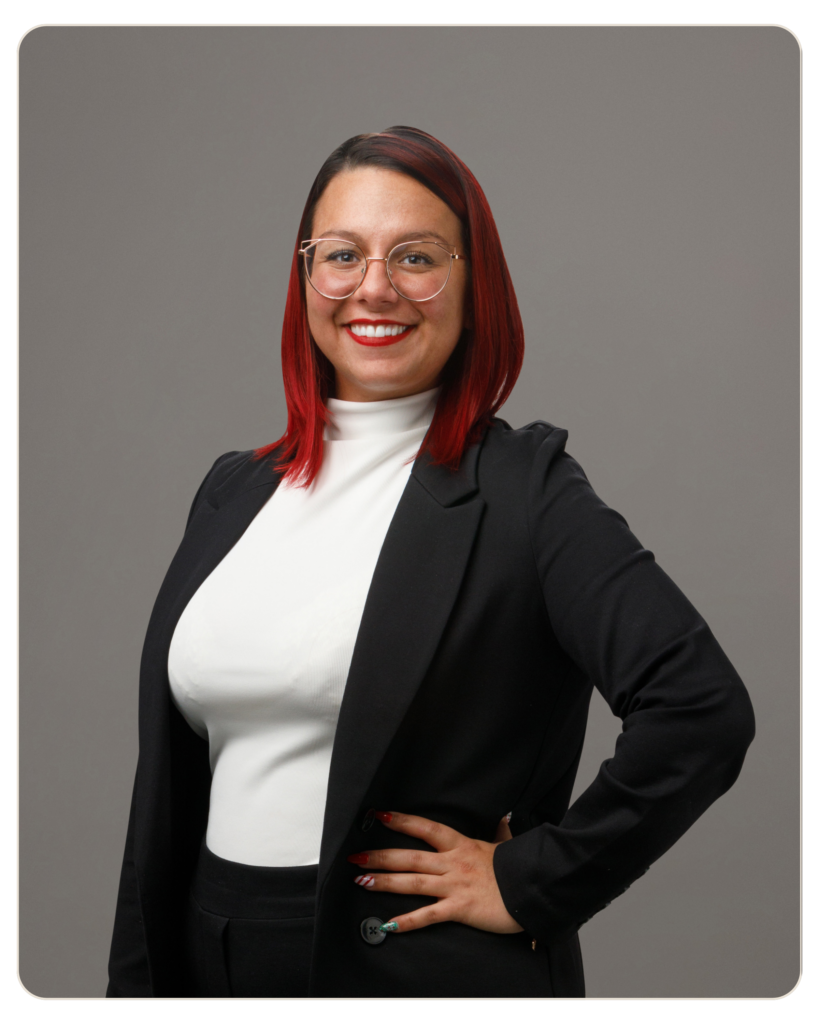 Kristina Mazzone, CAC Case Manager Professional woman with red hair and round glasses posing with hand on hip against a gray backdrop.